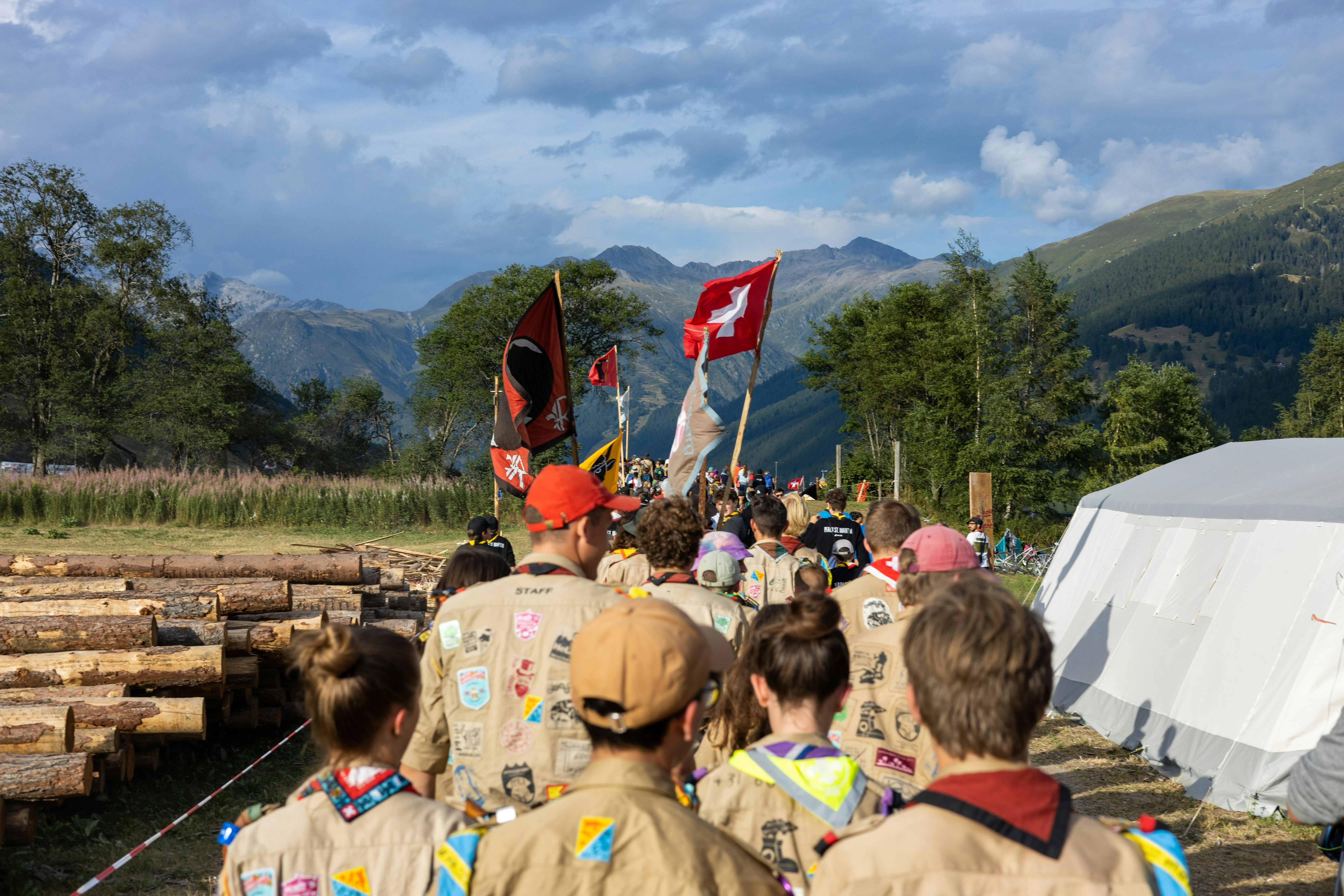 A procession of scouts parading with banners as they proceed on a trail between the mountains