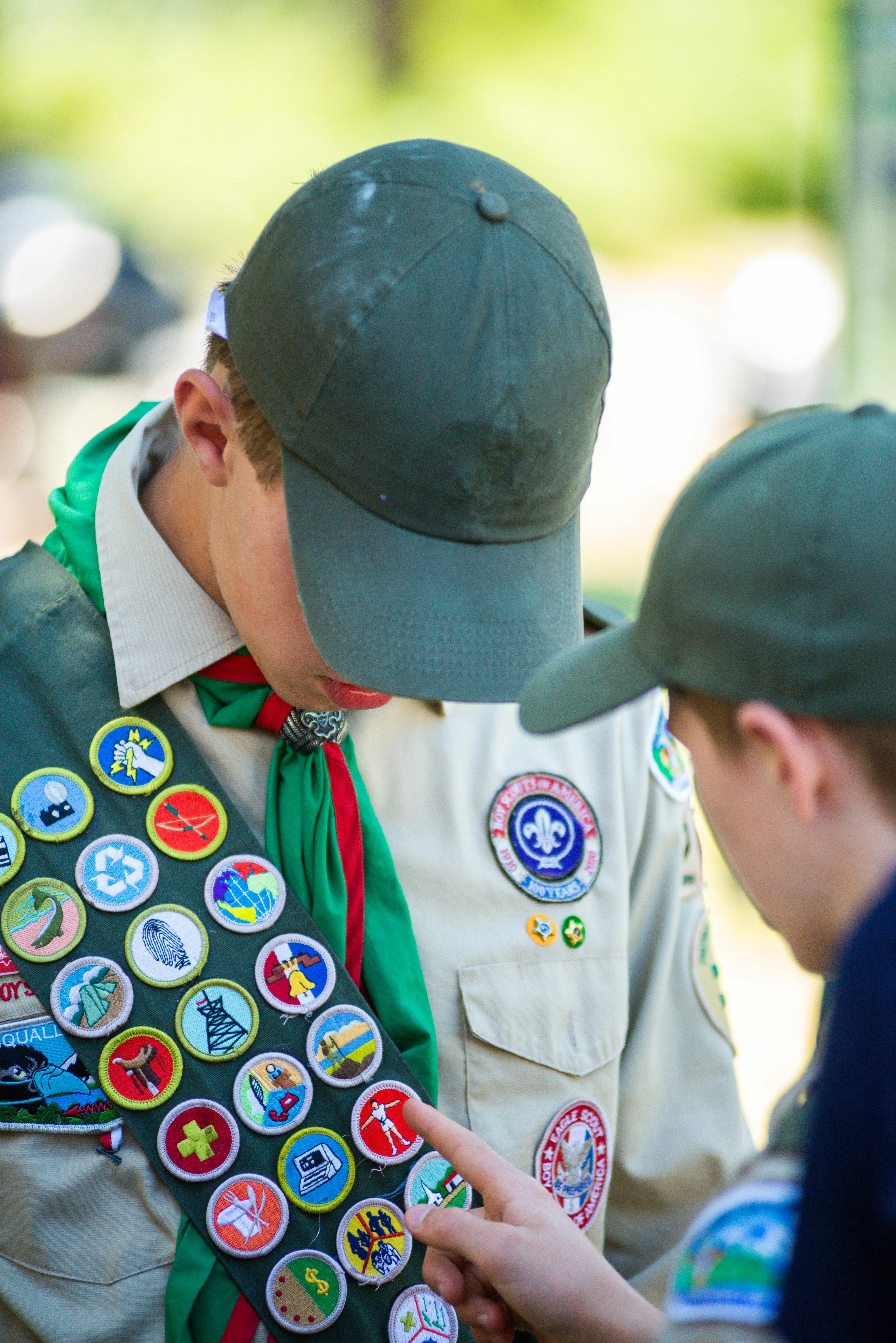 A scout pointing to the merit badges on the sash worn by another scout